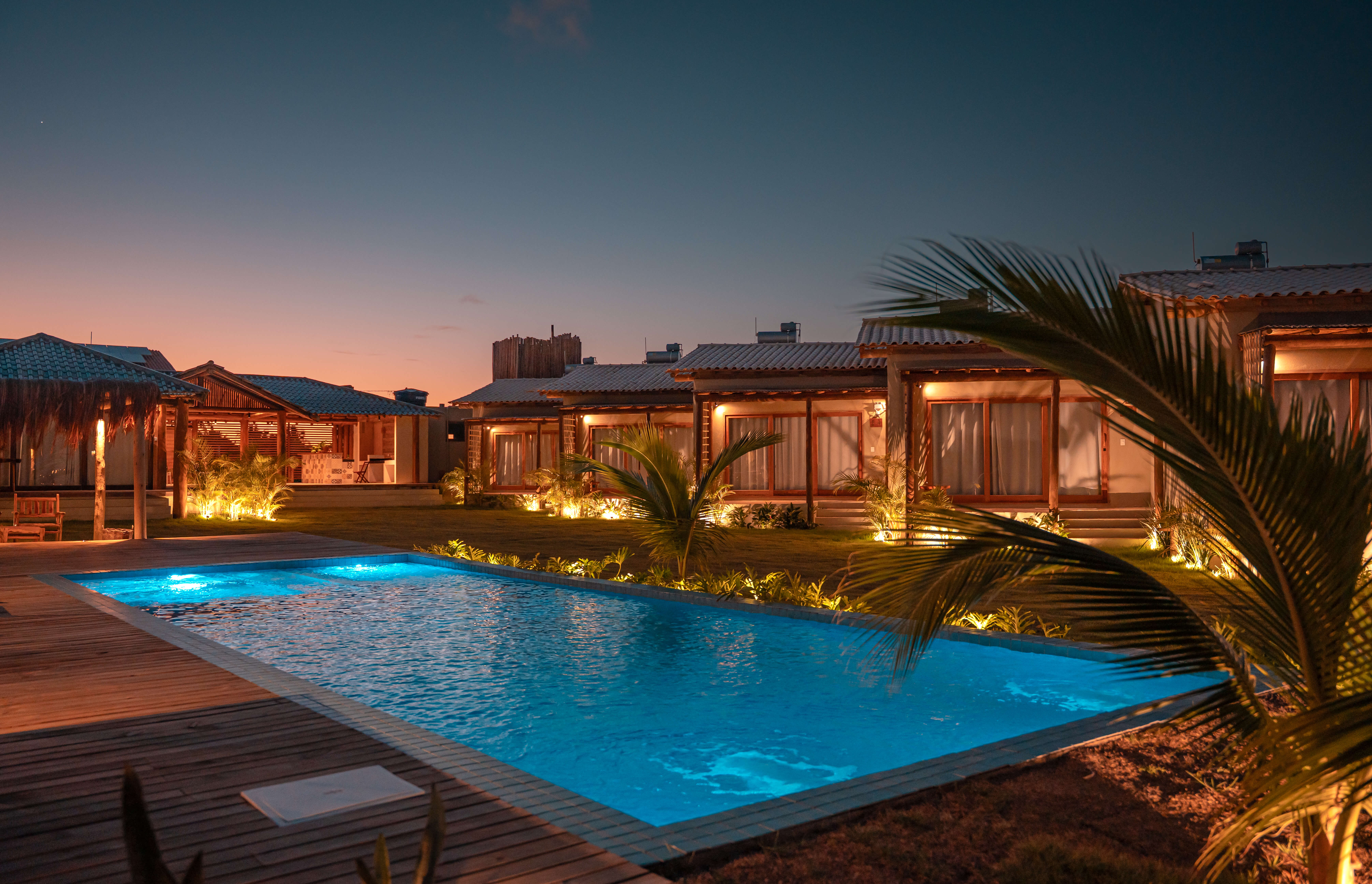 Falésias Orybá ao entardecer, com os chalés iluminados e a piscina refletindo o céu